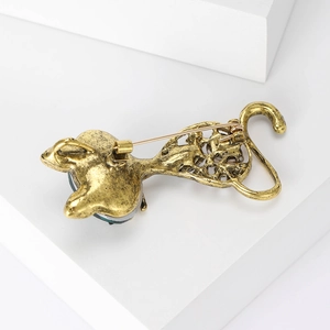 Detailed macro view of vintage gold cat brooch with intricate hollow patterns and green gem