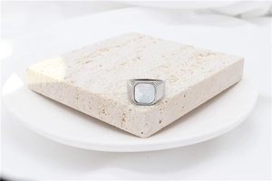 Minimalist silver ring with square white shell inlay on a natural stone display