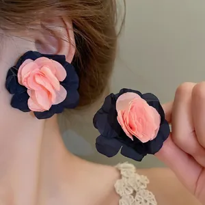 Detailed view of layered coral pink and navy blue fabric flower earrings on model