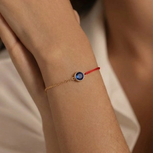 Elegante bracciale a catena dorata e cordino rosso con uno zircone blu centrale