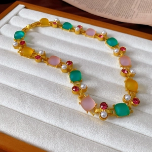 Detail of vintage palace style necklace with colorful square stones and pearls on white tray