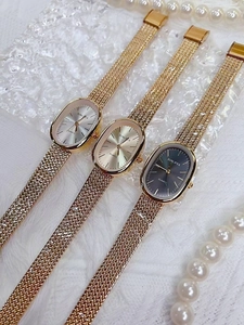 Three elegant oval quartz watches with mesh bands and pearls on white texture