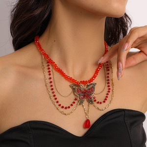 Detail of multi-layered gold necklace with red glass beads and rhinestone butterfly pendant