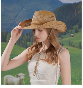 Brown woven straw cowboy hat with wide brim and adjustable chin strap in rural scenery
