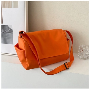 Detail view of the vibrant orange messenger bag with side pockets on a white podium