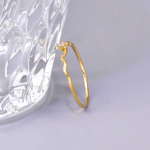 Minimalist wavy gold ring with a sparkling round diamond set against a glass cup
