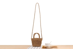 Detail of light brown woven straw crossbody bag with dual handles and long shoulder strap
