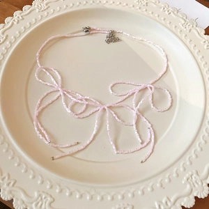 Close-up of pink square beaded necklace with bow tie design on vintage ceramic plate
