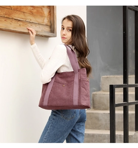 Canvas tote bag in purple-red worn over the shoulder by a model in a natural setting