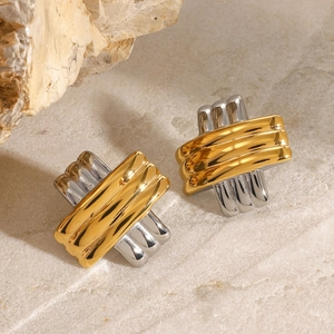 Detailed view of two-tone wavy crossed stud earrings on a beige marble stone surface