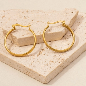 Detail of gold hoop earrings with brushed metal texture on travertine stone background