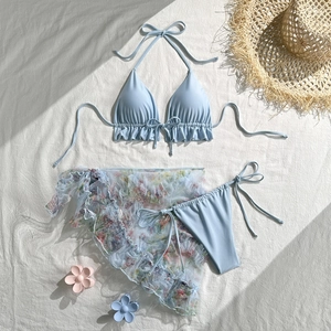 Flat lay of light blue ruffle bikini with floral mesh sarong and summer accessories