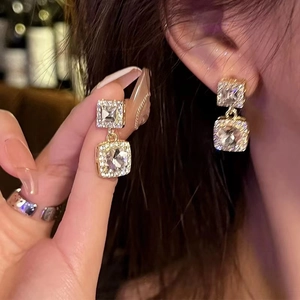 Close-up of square pearl earrings with gold-plated zircon crystals on earlobe
