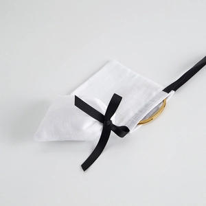 Detail of gold crystal bracelet next to white linen drawstring pouch with black ribbon bow