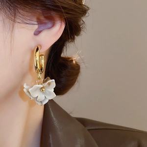 Close-up of a model wearing a gold hoop earring with a white resin flower petal pendant