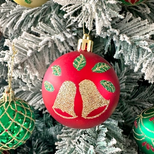 Detail of red matte Christmas ball with gold glitter bells hanging on a snowy pine tree