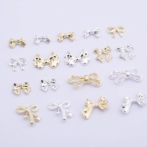 Detailed view of silver and gold alloy bow-knot nail art charms on a lavender background