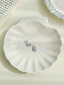 Detail of shell and crystal stud earrings displayed on a white decorative shell tray