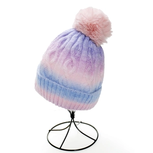 Close-up of cable knit texture and pink faux fur pompom on gradient winter beanie