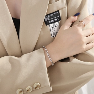 Close-up of interlocking silver chain bracelet and gold square diamond ring on a model