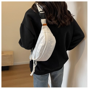 Detail view of a white canvas chest bag featuring an adjustable black strap and rope zippers