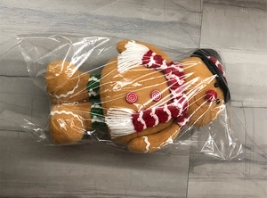Detail of Christmas gingerbread man plush toy with scarf and hat in clear packaging