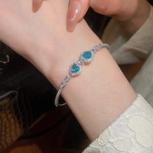 Detail of luxury zircon silver bracelet featuring two blue heart gems on model wrist