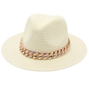 Détail d'un chapeau de paille beige avec une chaîne métallique épaisse en or rose