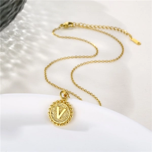 Macro view of gold stainless steel necklace with circular pendant featuring letter V detail