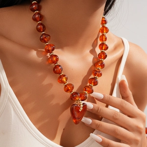 Macro shot of amber acrylic beaded necklace featuring a large heart pendant and gold accents