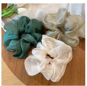 Three-piece set of large silk texture scrunchies in green, champagne, and white on wood