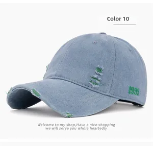 Detail of light blue distressed denim cap with green 1999 embroidery and torn fabric