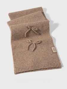 Close-up of brown knit scarf featuring bow accents and a premium UCC leather brand label