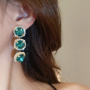 Close-up of elegant gold earrings with three emerald gemstones and crystal accents
