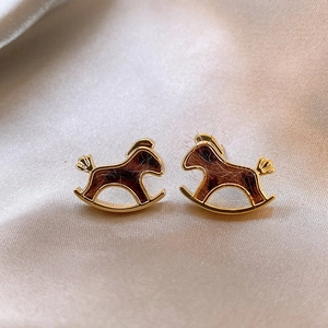 Detailed macro view of 18K gold-plated pony stud earrings on luxurious champagne silk fabric