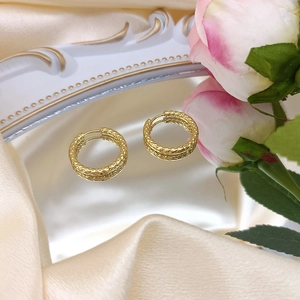 Close-up of golden textured hoop earrings on elegant champagne silk with roses