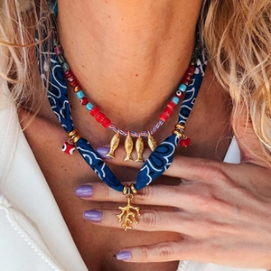 Detail of layered bohemian necklace with red beads, blue fabric, and gold coral pendants