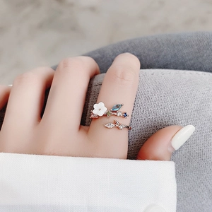 Detail shot of a rose gold floral ring with blue crystals and white flower on hand