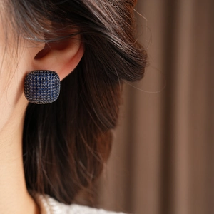 Close-up of square blue zircon earrings with pave setting worn on an earlobe