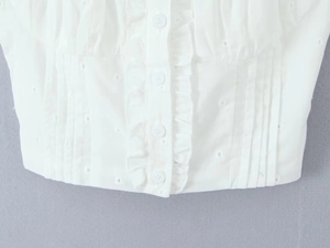 Close-up of white vest with ruffle trim, embroidery details and small white buttons