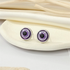 Detail of purple glitter resin evil eye studs on a minimalist off-white tray with silk