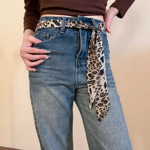 Close-up of high-waisted blue jeans with a stylish leopard print silk scarf belt detail