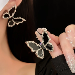 Close-up of black and gold butterfly earrings with silver needles worn by a model