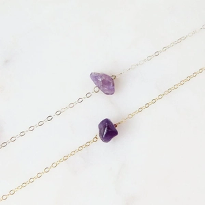 Macro detail of two golden cross chains featuring irregular purple amethyst gemstones