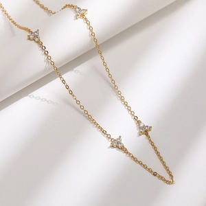 Macro detail of gold-tone choker necklace with delicate clover pendants and clear zircons