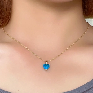 Detail of a blue heart-shaped birthstone pendant on a gold chain worn on the neck