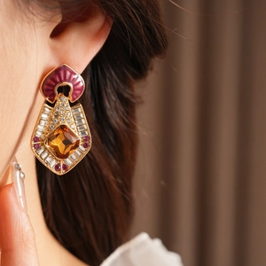 Close-up of vintage gold earrings with purple enamel, sparkling rhinestones and amber gems