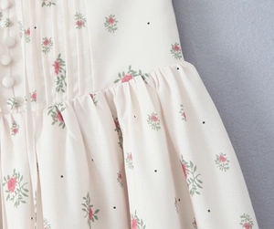 Detail of floral dress with red roses, black dots, and fabric-covered buttons on beige linen