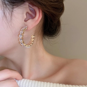 Detailed view of a gold-tone C-shaped hoop earring with sparkling pavé-set zircons on a model