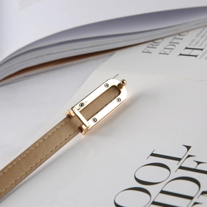 Dettaglio della sottile cintura in pelle beige con fibbia d'oro e cuciture fini